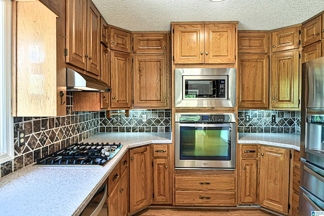 5000 Cameron Rd, Birmingham, AL 35242 - kitchen featuring brown cabinets, under cabinet range hood, light countertops, backsplash, and appliances with stainless steel finishes