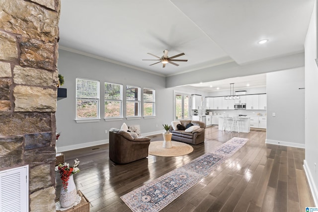 living area featuring baseboards, a stone fireplace, a ceiling fan, crown molding, and dark wood-type flooring