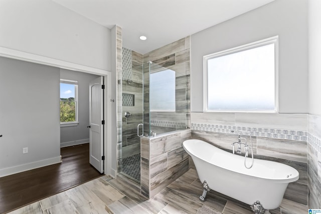 bathroom featuring baseboards, a stall shower, a freestanding bath, tile walls, and wood finished floors
