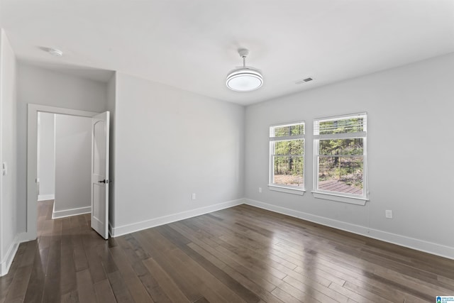 empty room featuring dark wood-type flooring, visible vents, and baseboards