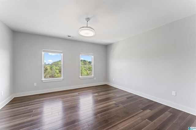 unfurnished room featuring visible vents, dark wood-style flooring, and baseboards