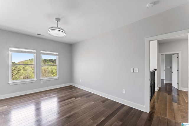 empty room with dark wood-style flooring, visible vents, and baseboards