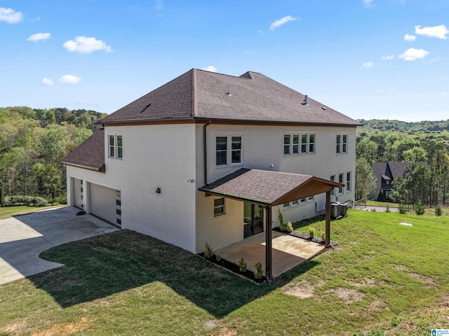 back of property with a lawn, a patio, concrete driveway, brick siding, and roof with shingles