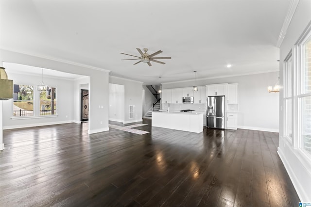 unfurnished living room with dark wood-style flooring, baseboards, ornamental molding, stairs, and ceiling fan with notable chandelier