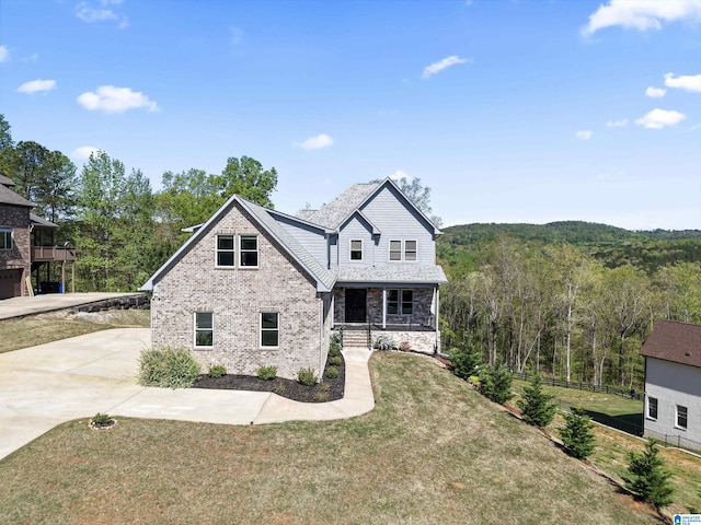 view of front of home with a porch, a forest view, a front yard, and stone siding