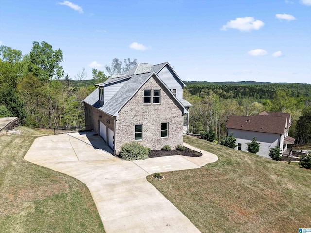 view of property exterior with a wooded view, driveway, a yard, and brick siding