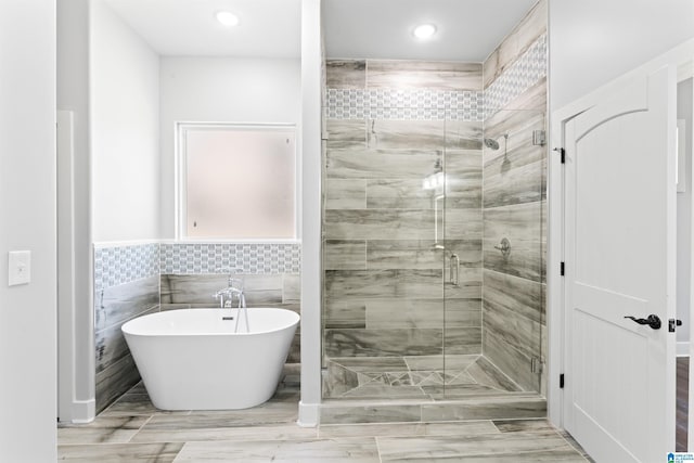 bathroom with wainscoting, tile walls, a stall shower, and a soaking tub