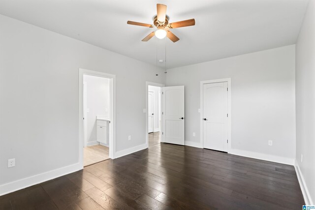 unfurnished bedroom with dark wood-style flooring, ensuite bathroom, baseboards, and ceiling fan