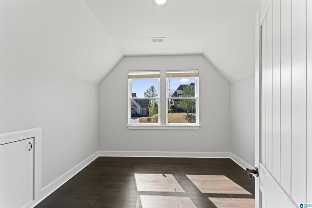 additional living space with lofted ceiling, visible vents, baseboards, and dark wood-style floors