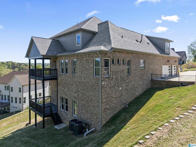view of side of home with a shingled roof, a lawn, central AC unit, and brick siding