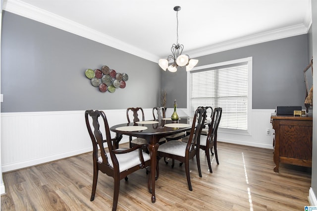 dining room with ornamental molding, light wood-type flooring, an inviting chandelier, and wainscoting