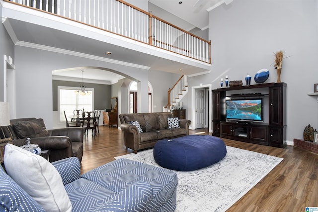 living area with arched walkways, wood finished floors, crown molding, and a towering ceiling