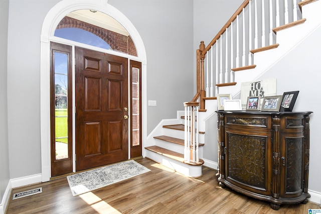 foyer with stairs, visible vents, baseboards, and wood finished floors