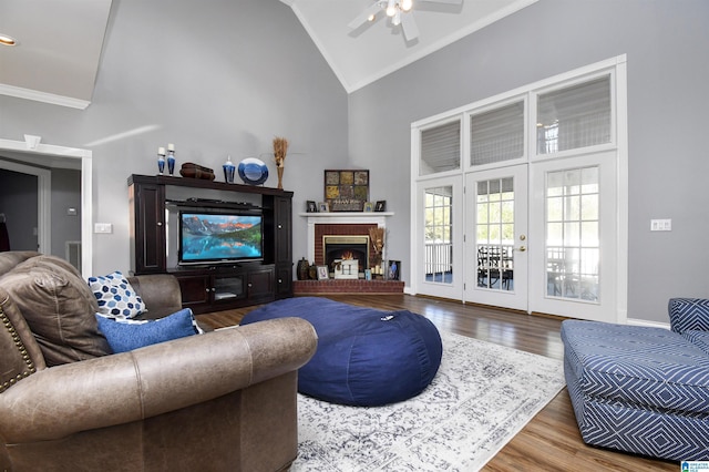 living room featuring high vaulted ceiling, ceiling fan, ornamental molding, wood finished floors, and a brick fireplace