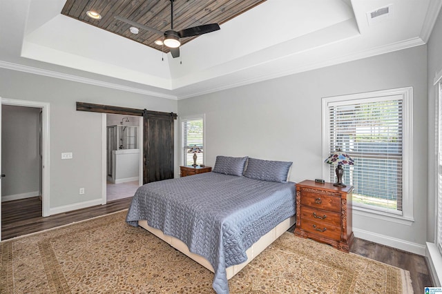 bedroom with a barn door, a tray ceiling, and wood finished floors