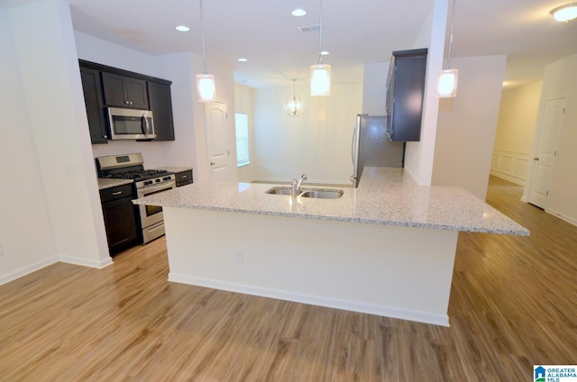 kitchen featuring a sink, light wood-style floors, a peninsula, appliances with stainless steel finishes, and light stone countertops