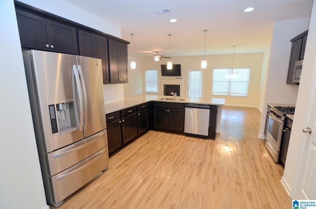 kitchen with light stone counters, a ceiling fan, a sink, light wood-style floors, and stainless steel appliances