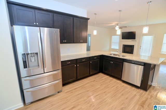 kitchen featuring stainless steel appliances, a sink, light wood-type flooring, light stone countertops, and ceiling fan