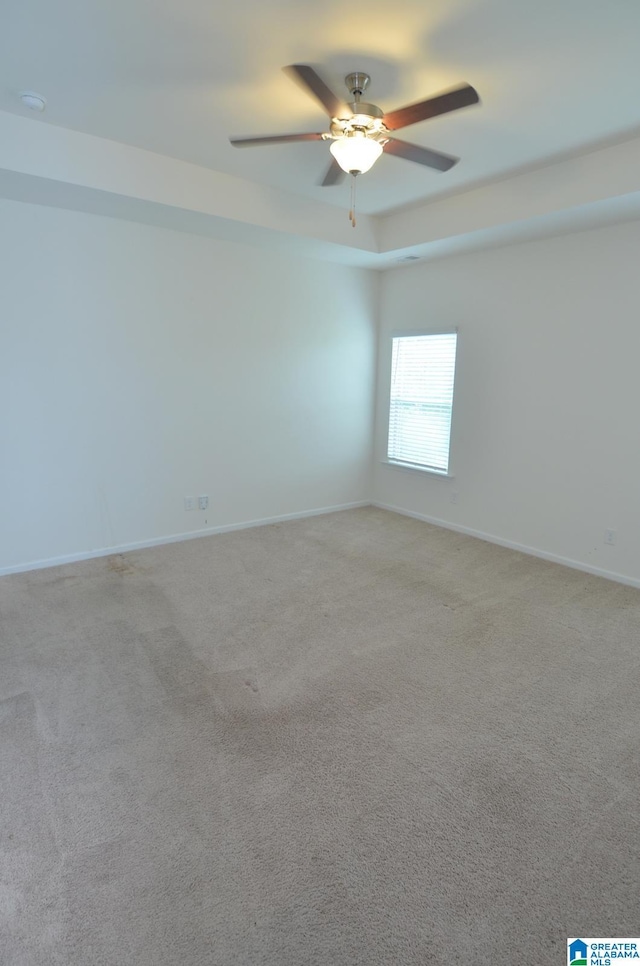 spare room with baseboards, light colored carpet, ceiling fan, and a tray ceiling