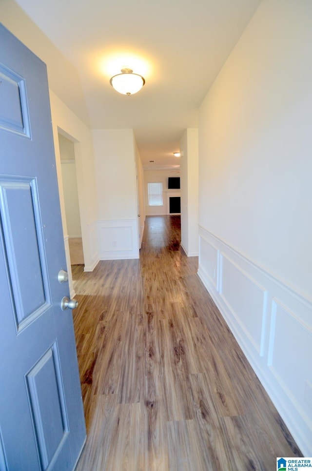hallway with wainscoting, wood finished floors, and a decorative wall
