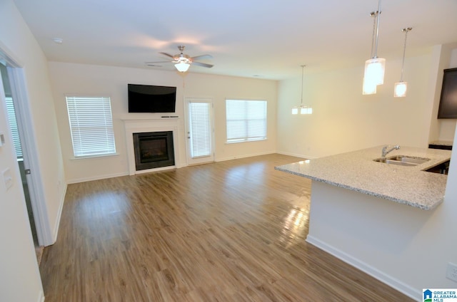 unfurnished living room featuring a sink, baseboards, light wood-style floors, a ceiling fan, and a fireplace