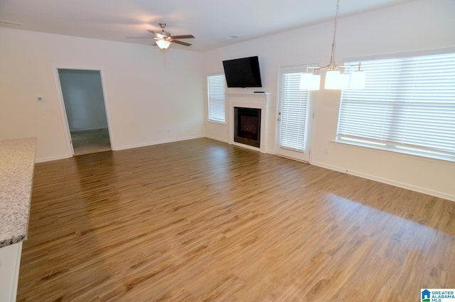 unfurnished living room featuring a fireplace, baseboards, wood finished floors, and ceiling fan with notable chandelier