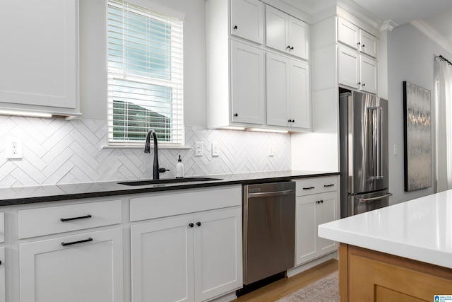 kitchen with white cabinetry, appliances with stainless steel finishes, a sink, dark countertops, and decorative backsplash