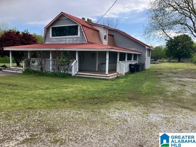 rear view of property featuring covered porch, a gambrel roof, and a yard