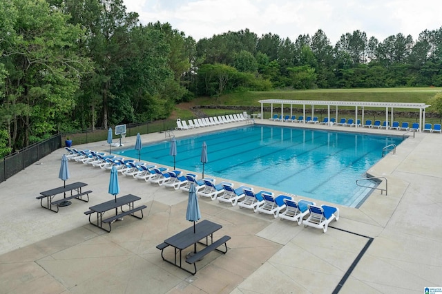 pool featuring a pergola, a patio, fence, and a wooded view