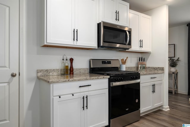 kitchen with white cabinetry, appliances with stainless steel finishes, light stone counters, and wood finished floors