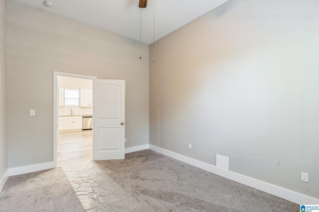 spare room featuring light colored carpet, baseboards, and a ceiling fan