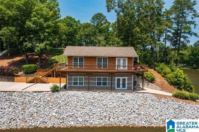 view of front of house with french doors, a deck with water view, and a patio