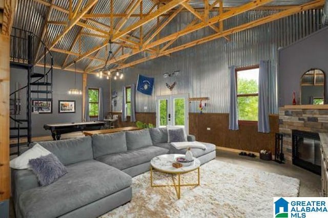 living area featuring a stone fireplace, high vaulted ceiling, stairs, and a healthy amount of sunlight