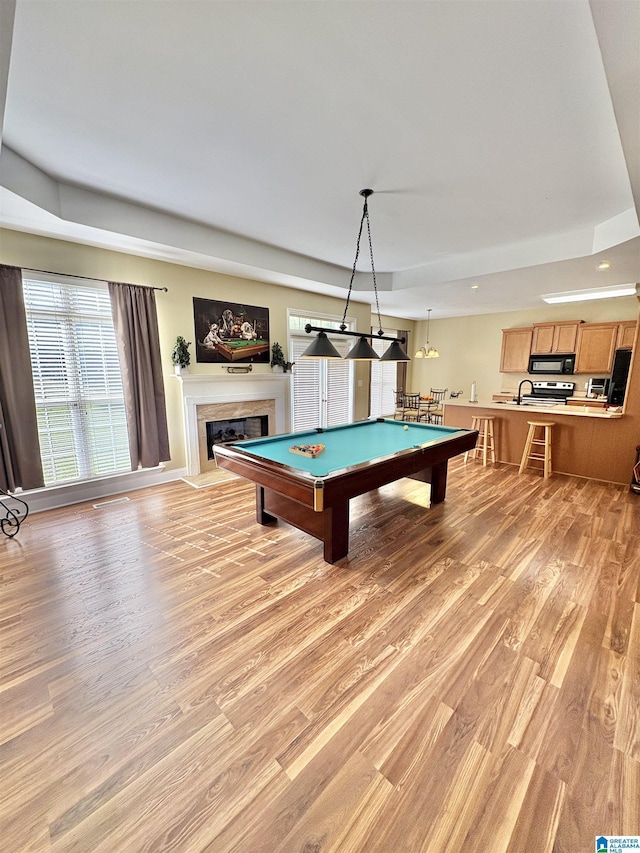 rec room featuring pool table, recessed lighting, a fireplace with flush hearth, a raised ceiling, and light wood finished floors