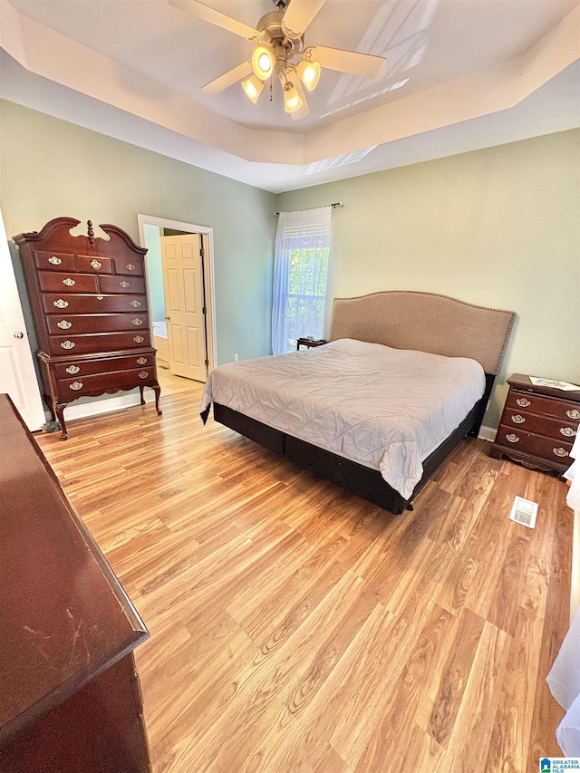 bedroom featuring light wood-style flooring, ceiling fan, and a raised ceiling