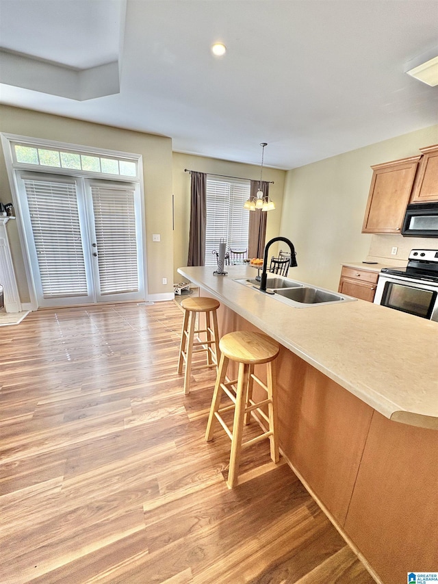 kitchen featuring light wood-style floors, black microwave, a kitchen bar, stainless steel electric range oven, and a sink