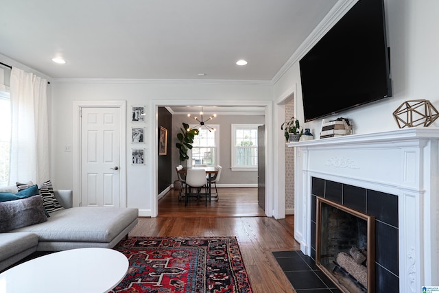 living area featuring an inviting chandelier, a tiled fireplace, baseboards, ornamental molding, and dark wood finished floors