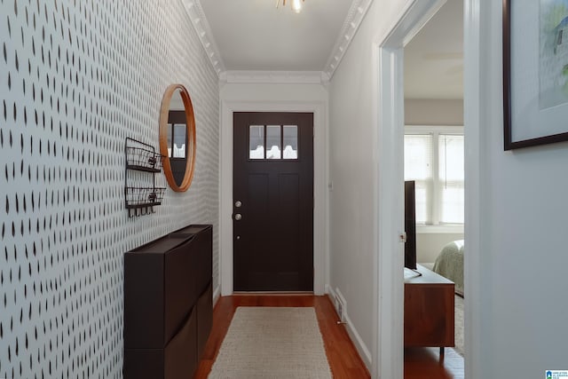 doorway featuring wood finished floors, wallpapered walls, baseboards, visible vents, and crown molding