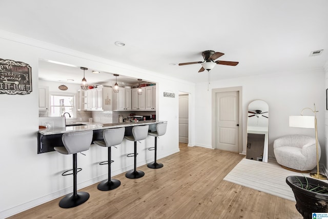 kitchen featuring a kitchen bar, a ceiling fan, visible vents, and a sink