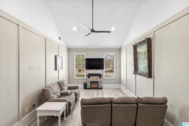 living area featuring vaulted ceiling, a stone fireplace, light wood finished floors, visible vents, and a ceiling fan