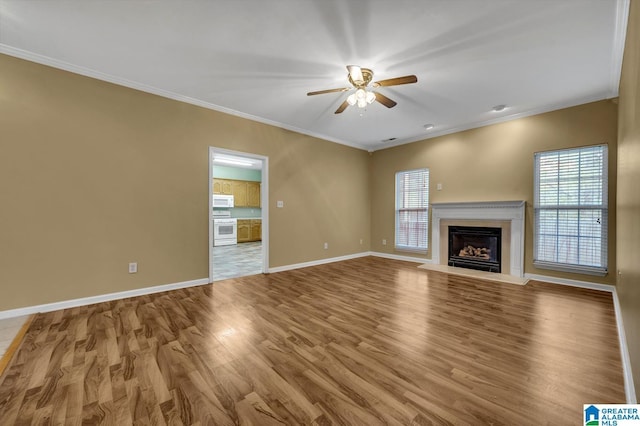 unfurnished living room featuring wood finished floors, ornamental molding, a ceiling fan, and a wealth of natural light