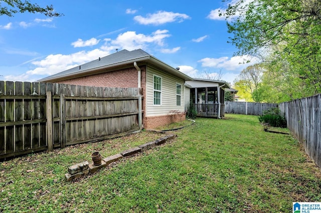 exterior space featuring brick siding, a fenced backyard, a sunroom, and a lawn
