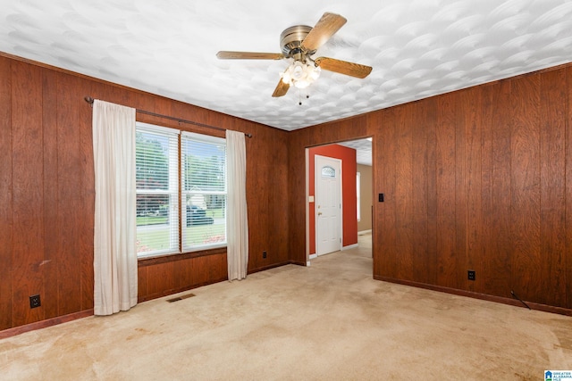 carpeted spare room with wooden walls, visible vents, baseboards, and ceiling fan