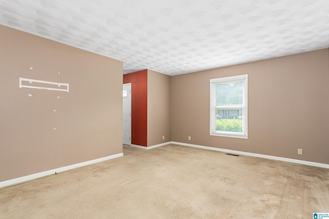 spare room with light carpet, baseboards, visible vents, and a textured ceiling