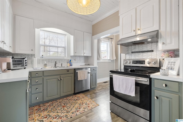 kitchen featuring ornamental molding, light countertops, white cabinets, under cabinet range hood, and stainless steel appliances