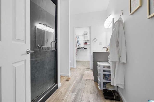 full bath with vanity, wood finished floors, a walk in closet, a stall shower, and baseboards
