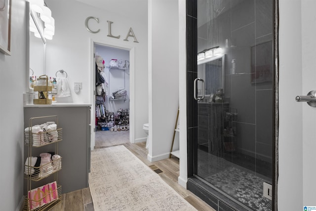 bathroom featuring a spacious closet, a stall shower, and wood finished floors