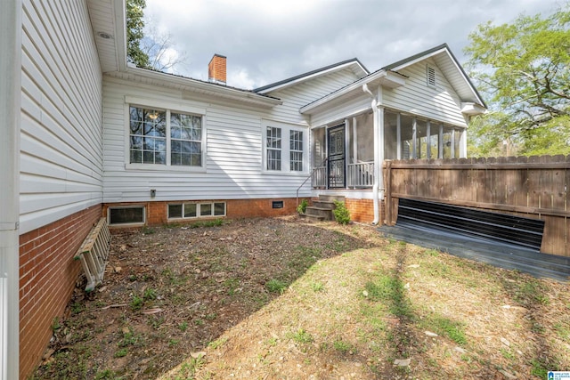 view of side of home featuring a sunroom, a chimney, and fence