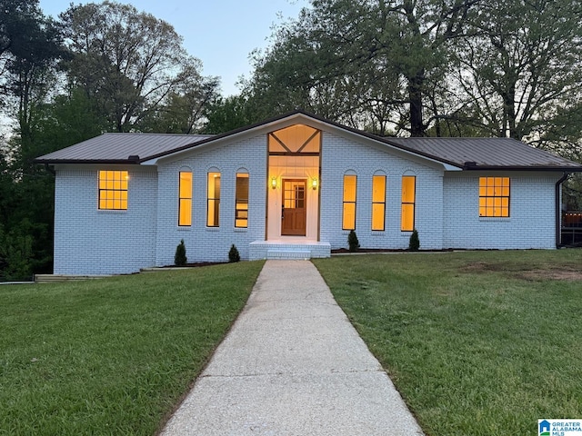 view of front of property with metal roof, a standing seam roof, a front lawn, and brick siding
