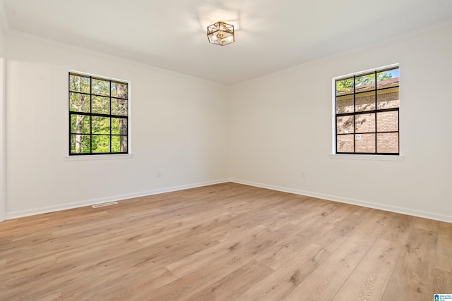 empty room featuring light wood-style flooring, visible vents, crown molding, and baseboards